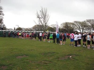 A photograph showing a long queue of people waiting to use the temporary toilets at an outdoor event.